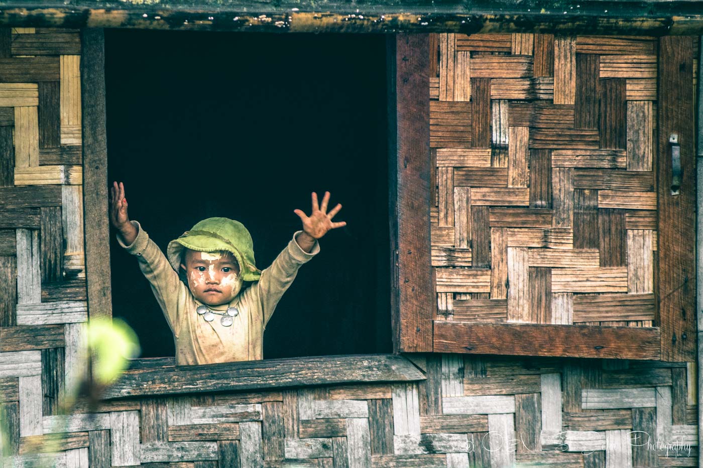 Burmese boy greets passers by from the window of his house in a hill tribe village in Myanmar